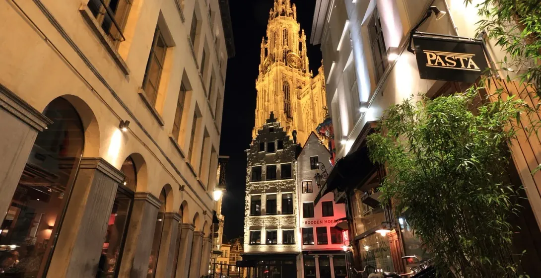 La Catedral de Amberes iluminada por la noche, vista desde una encantadora calle con restaurantes.