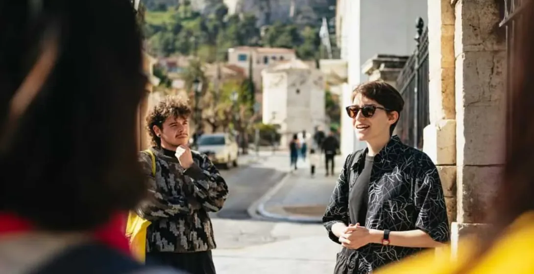 Un guía turístico conduce a un pequeño grupo por las encantadoras calles de Atenas, con la Acrópolis al fondo.