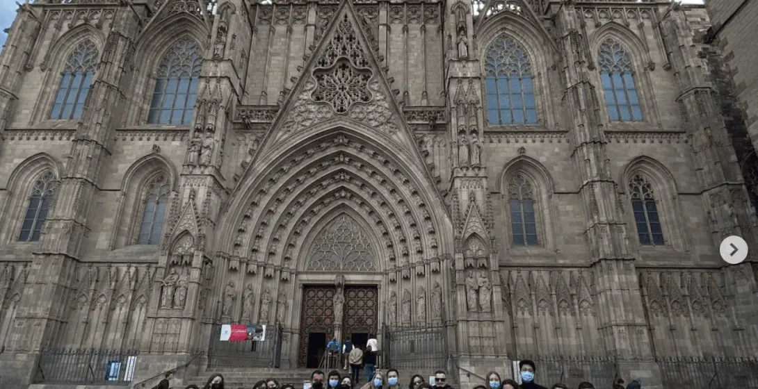 Un grupo de personas, muchas con mascarillas, posa frente a la ornamentada fachada gótica de la Catedral de Barcelona.