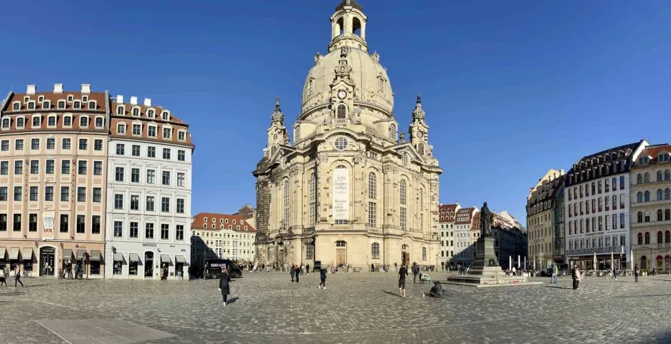 Panoramiczny widok na drezdeński plac Neumarkt z Frauenkirche, otoczony historycznymi budynkami i spacerującymi ludźmi.