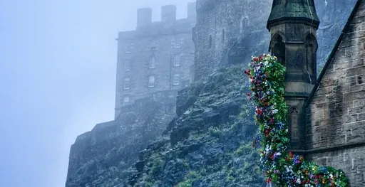 Castillo de Edimburgo envuelto en niebla, con un edificio decorado con flores en primer plano.