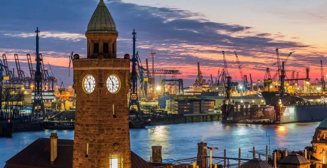 Puerto de Hamburgo al atardecer, con una torre del reloj y un paisaje industrial.
