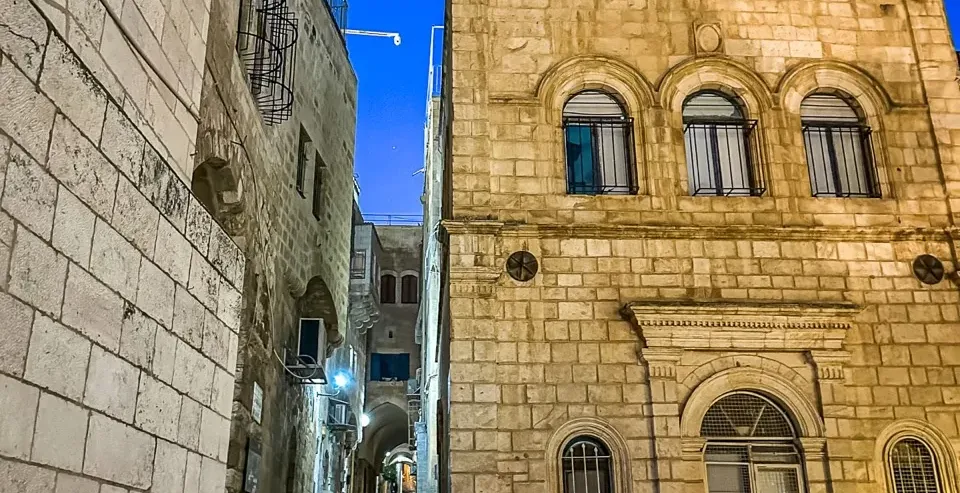 Una persona baja por una escalera de piedra en la iluminada Ciudad Vieja de Jerusalén por la noche.
