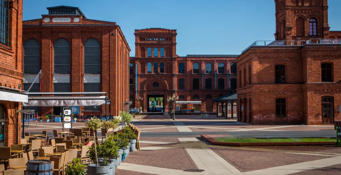 Ceglana architektura przemysłowa i brukowany plac z ogródkiem kawiarnianym pod czystym niebem w Łodzi.