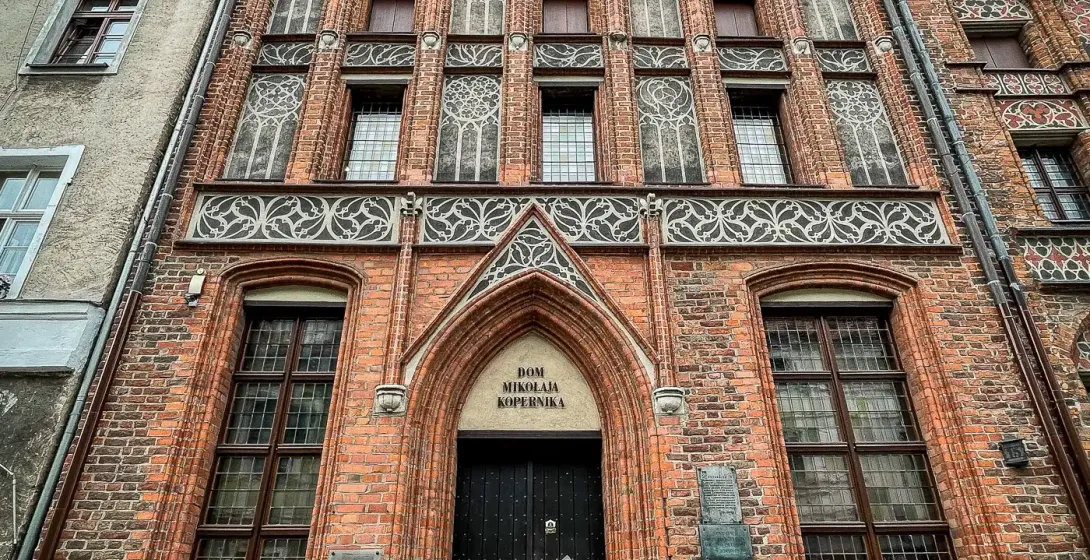 The Gothic brick House of Nicolaus Copernicus in Toruń, with a stepped gable roof and ornate windows, seen from below. A yell
