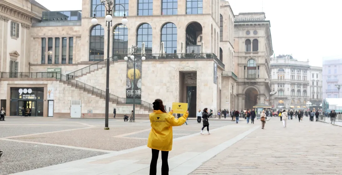 Tour guide in a yellow jacket holding a sign on Piazza del Duomo in Milan in front of the Museo del Novecento.