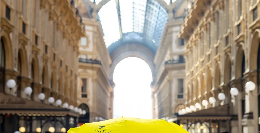 Tour guide holding an open yellow umbrella while leading a group inside Galleria Vittorio Emanuele II in Milan.