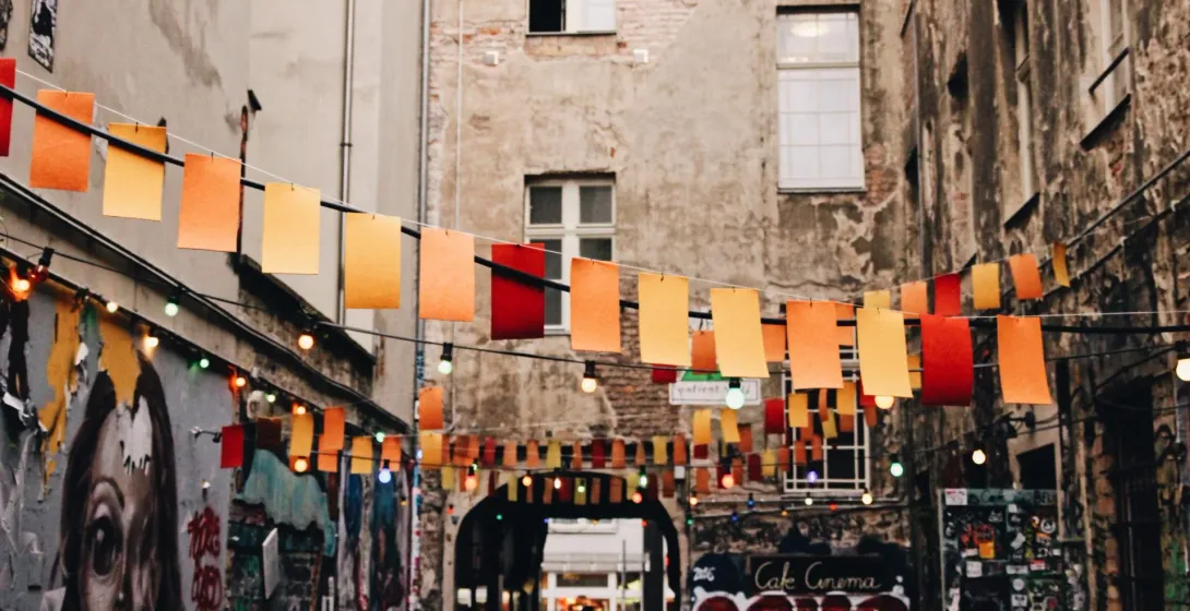 An alley in Berlin with street art and colorful flags and lights strung between weathered apartment buildings.