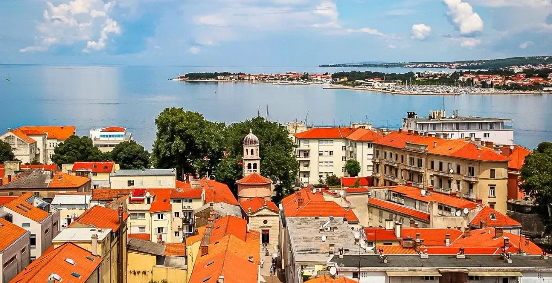 Widok z góry na Stare Miasto w Zadarze z pomarańczowymi dachami, kopułową dzwonnicą i Morzem Adriatyckim.