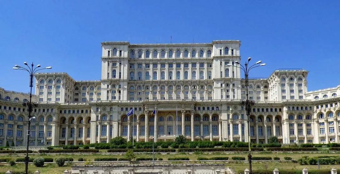 Exterior view of the Palace of the Parliament in Bucharest, Romania under a clear blue sky.