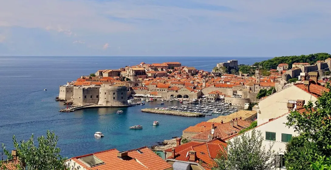 Panoramic view of Dubrovnik's old city walls, harbor, and terracotta rooftops under a blue sky.