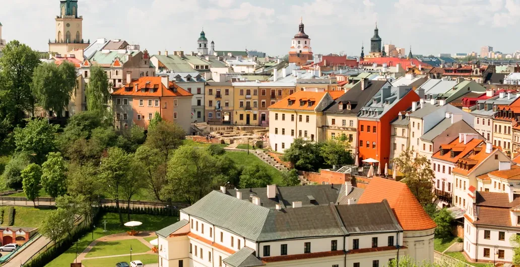 Panoramic view of Lublin's historic district with colorful buildings, churches, and green hillsides under a blue sky.