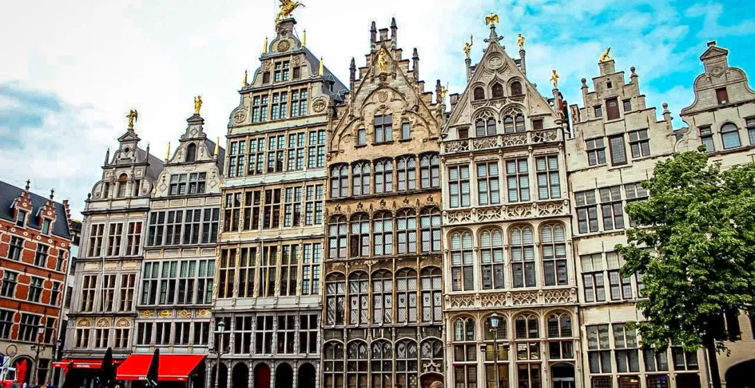 Historische Zunfthäuser mit Treppengiebeln und goldenen Statuen säumen einen Kopfsteinpflasterplatz in Antwerpen. Passanten g