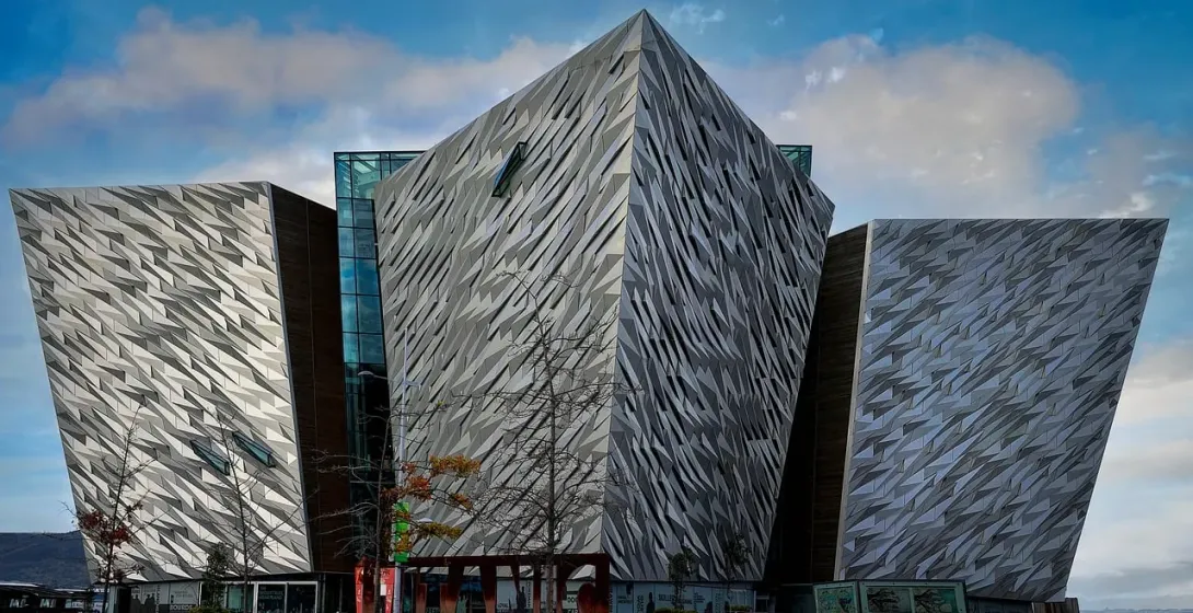 Budynek Titanic Belfast z kanciastymi, fasetowanymi srebrnymi panelami pod częściowo zachmurzonym niebem, z nagimi drzewami n