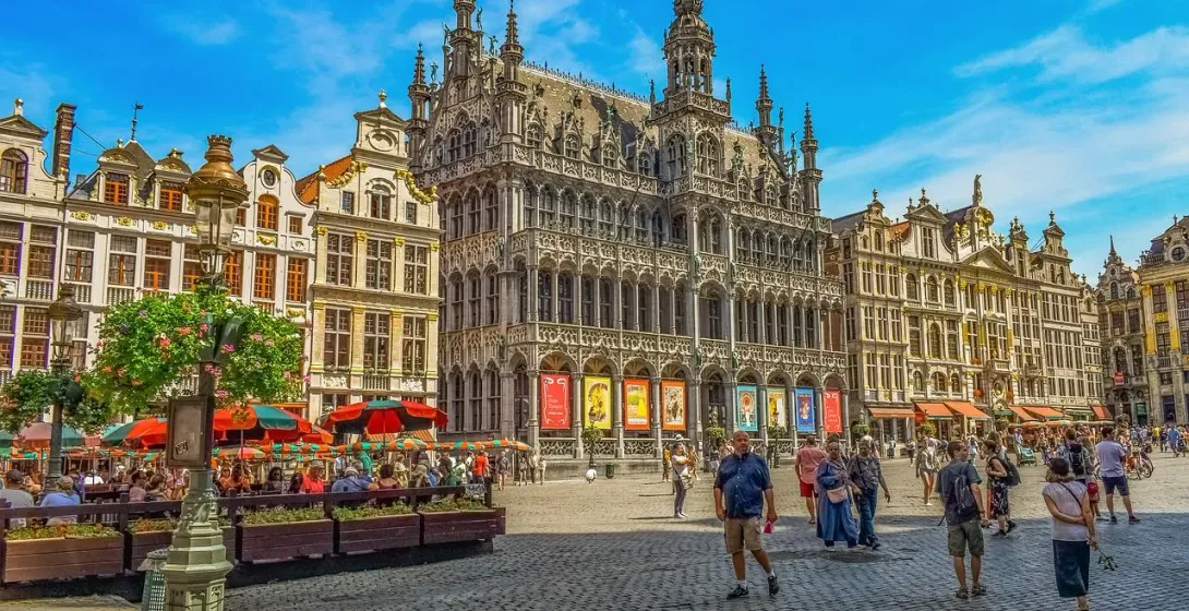 Wielki Plac w Brukseli z ozdobnymi zabytkowymi budynkami, kawiarniami na zewnątrz i ludźmi w słoneczny dzień.