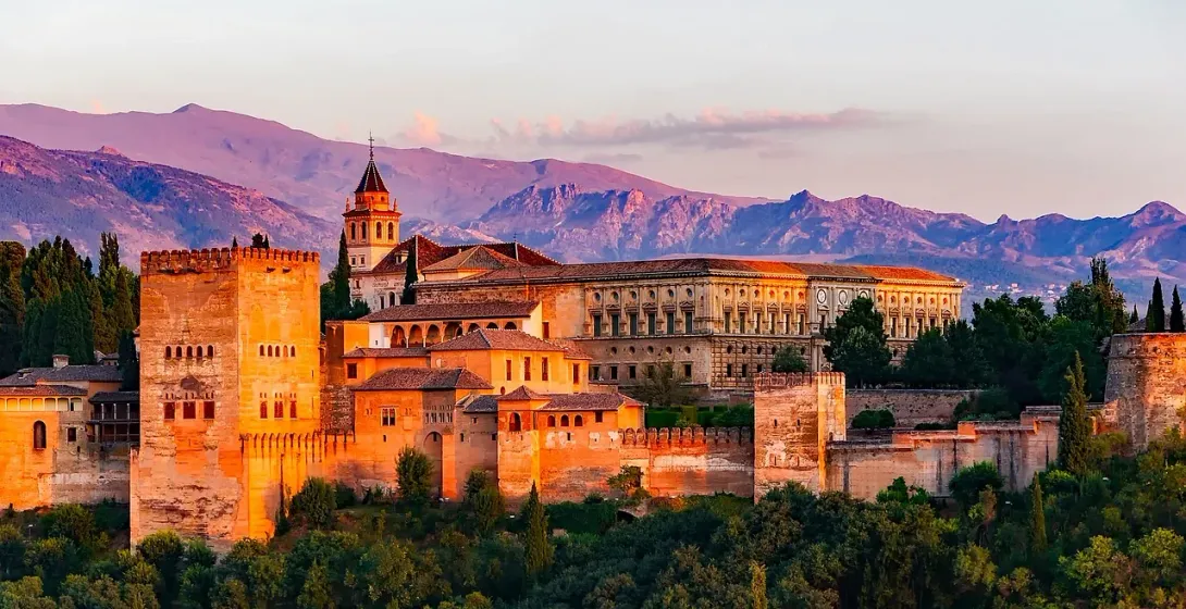 The Alhambra palace in Granada, Spain, glowing at sunset with mountains in the background.