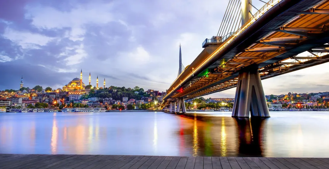 Istanbul's Golden Horn Metro Bridge illuminated at sunset, with the Suleymaniye Mosque visible on the historic skyline.