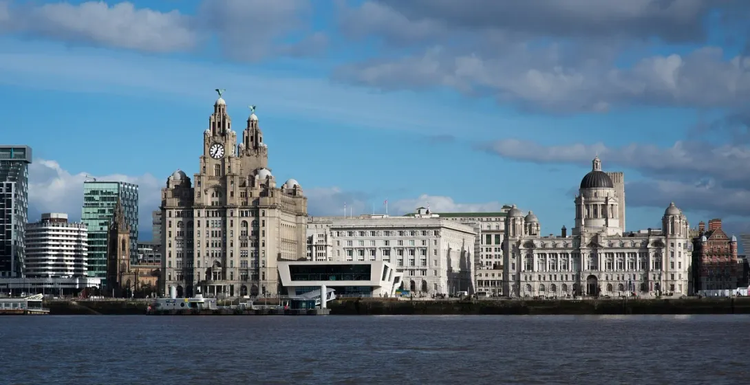 Nabrzeże Liverpoolu z Royal Liver Building, Cunard Building i Port of Liverpool Building pod częściowo zachmurzonym niebem.