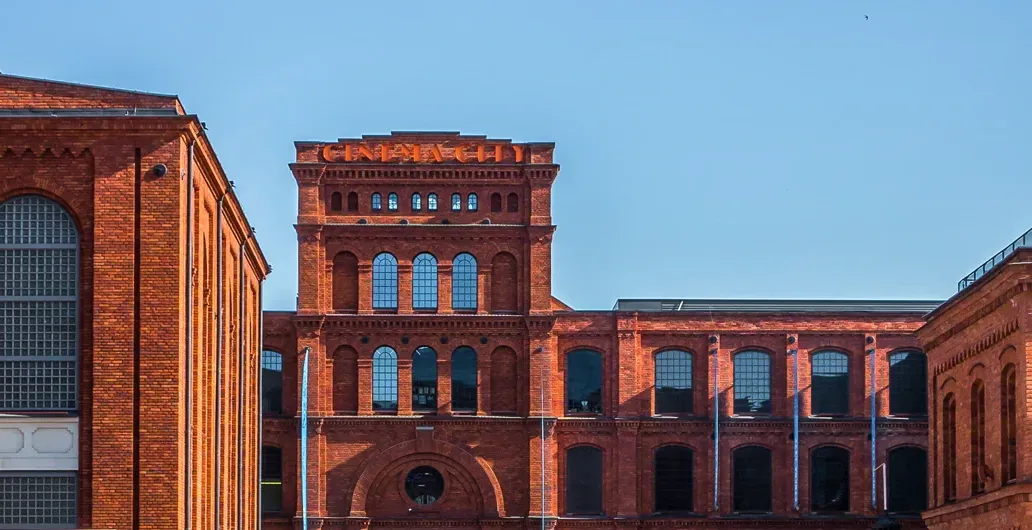 Panoramic view of red brick industrial architecture under a clear blue sky in Lodz, Poland, with arched windows.