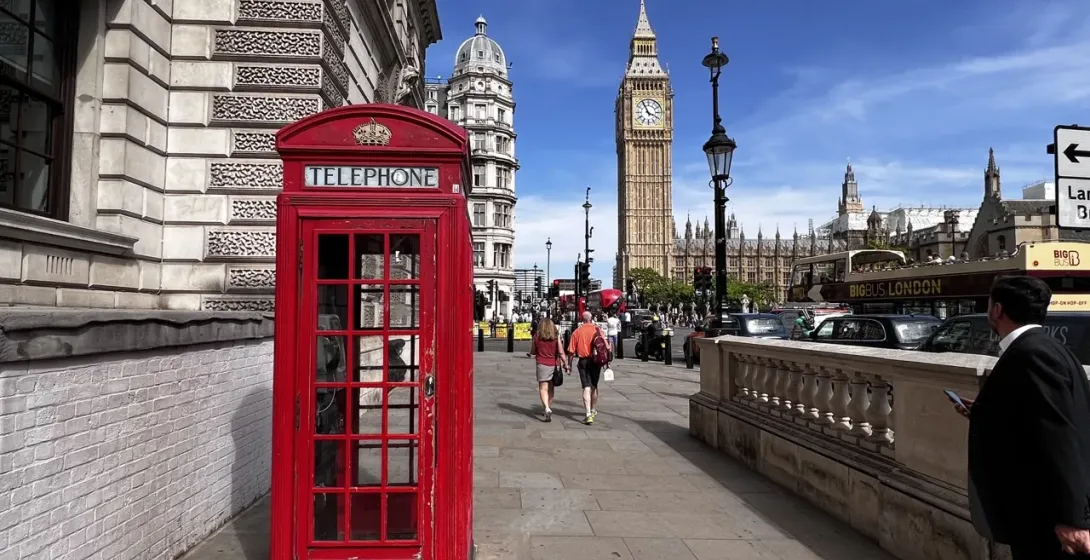 Classic red telephone booth on a London street, with Big Ben and the Houses of Parliament in the background.
