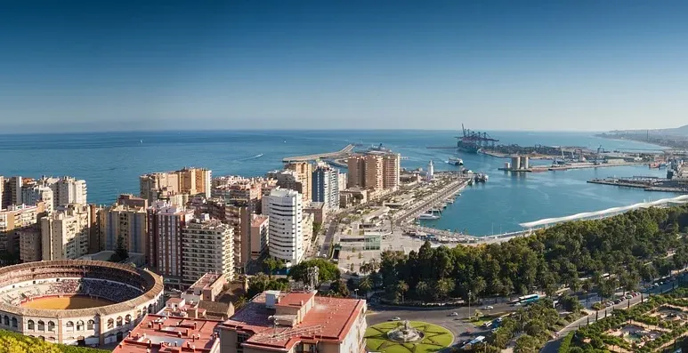 Panoramic view of Malaga, Spain, with the historic bullring, modern port, and Mediterranean Sea under clear skies.