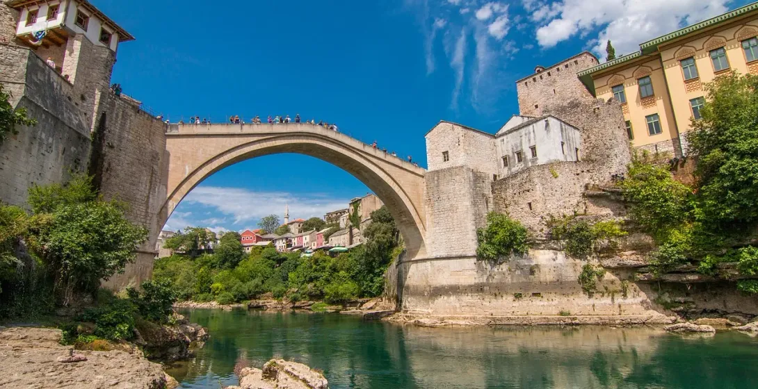 Historische Stari Most Brücke in Mostar, Bosnien und Herzegowina, über einem grünen Fluss, mit alten Steingebäuden und Uferve