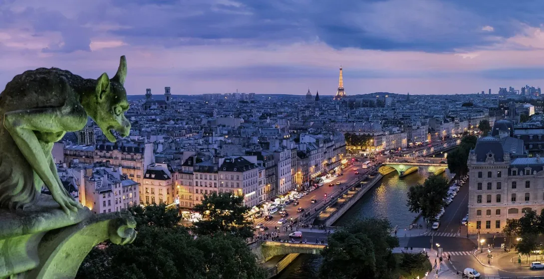 Stone gargoyle overlooking Paris skyline at dusk, Eiffel Tower visible in distance. City lights beginning to glow.