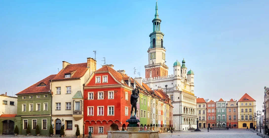 Cobblestone market square with a fountain and Apollo statue, colorful historic buildings, and a large town hall tower under a