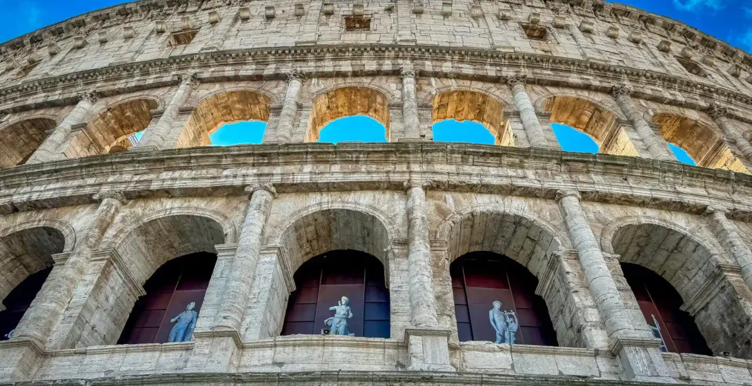 Vista exterior del Coliseo en Roma, mostrando múltiples niveles de arcos de piedra, columnas y estatuas en los arcos inferior