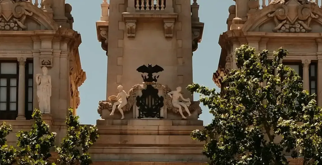 Full view of Valencia City Hall with central clock tower, flanked by domes, in a large, sunny square.