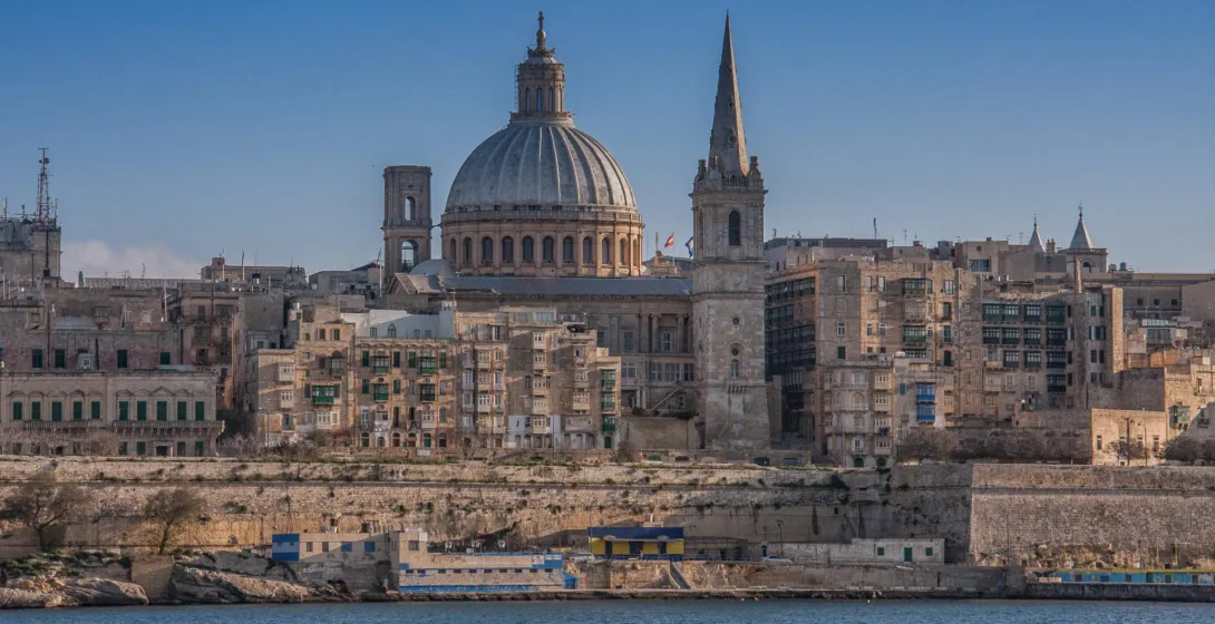 Valletta skyline with Grand Harbour, featuring a large cathedral dome and spire rising above historic buildings.