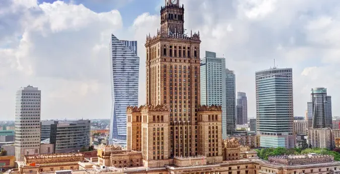 Aerial view of the Palace of Culture and Science and modern skyscrapers under a partly cloudy sky in Warsaw.