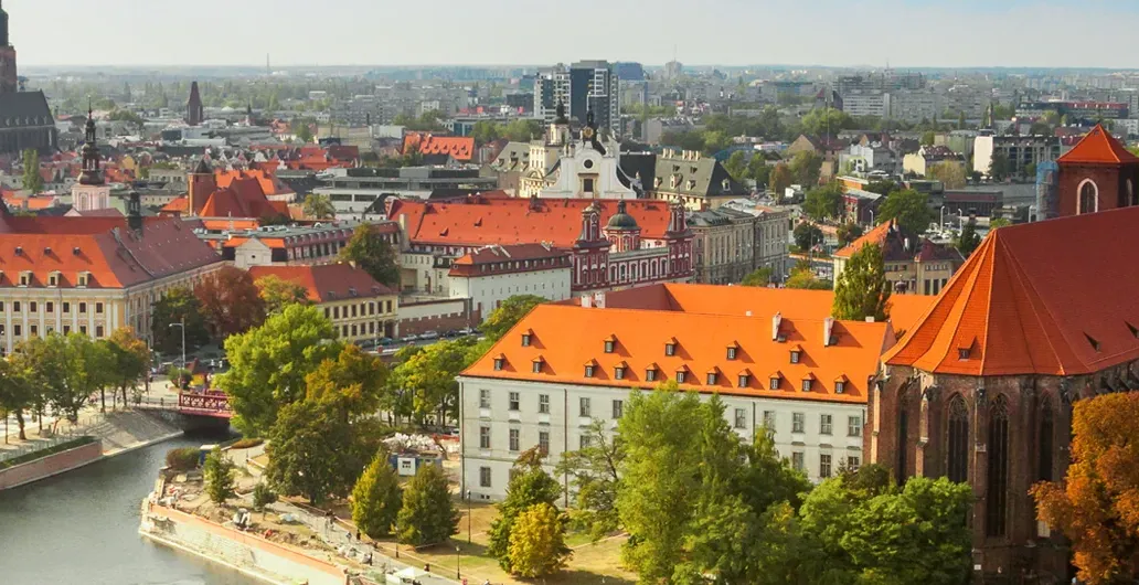 Panoramic view of Wroclaw, Poland, featuring the Odra River, historic red-roofed buildings, and city skyline.