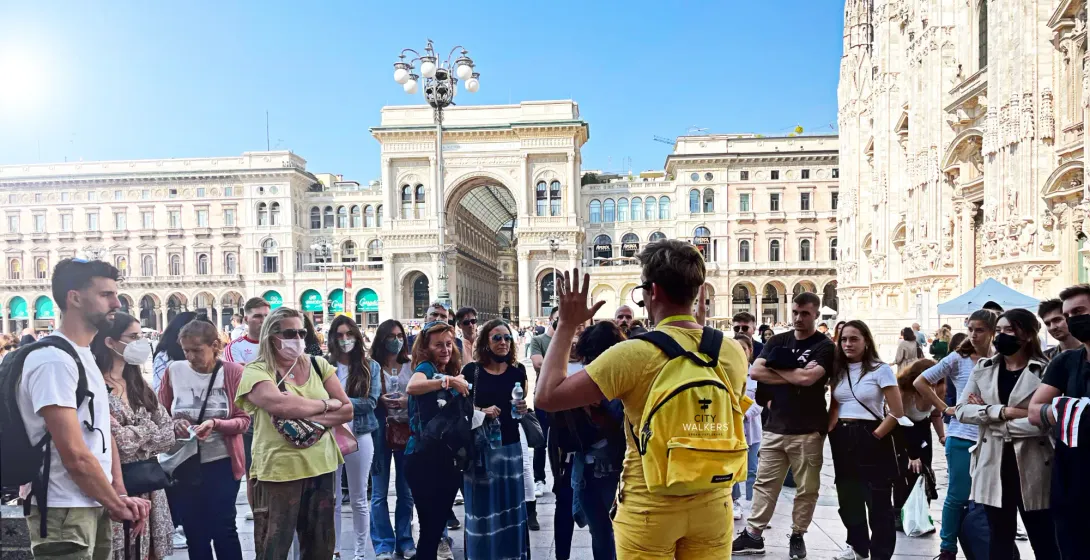 Tour guide in yellow speaking to a group of visitors on Piazza del Duomo in Milan.