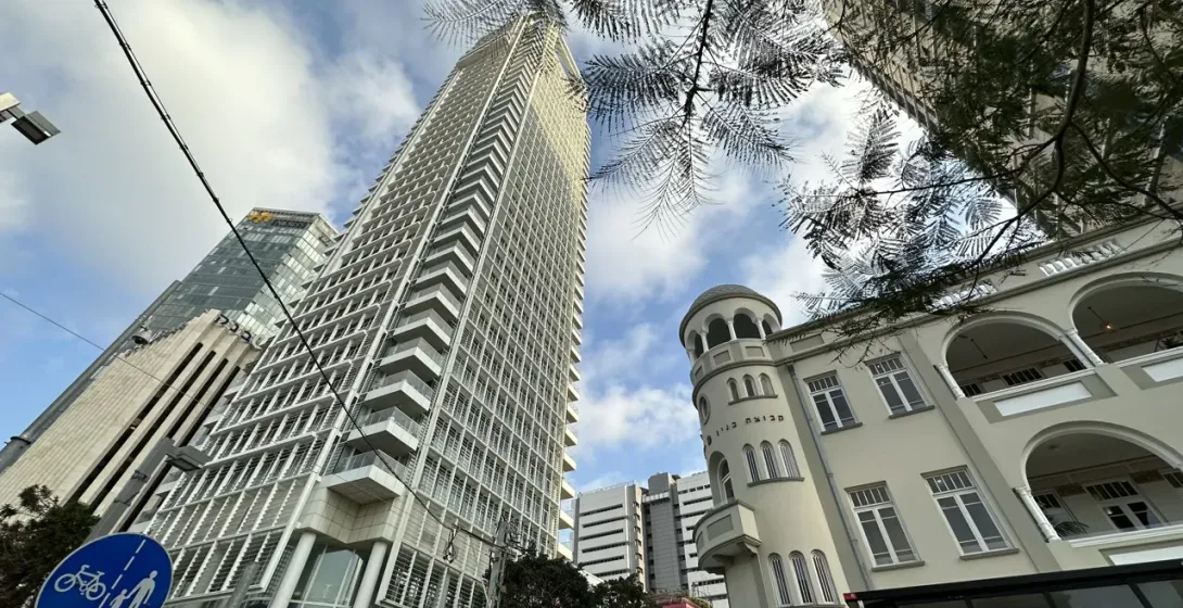 Hoher moderner Wolkenkratzer und älteres Gebäude mit Bögen und Rundturm, von unten in einer Straße von Tel Aviv gesehen.