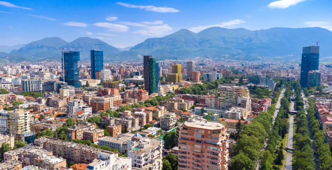 Panoramic view of Tirana, Albania, showing modern skyscrapers contrasting with older buildings and distant mountains.