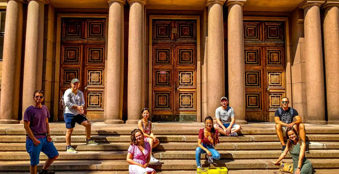 Wesoła grupa turystów pozuje na schodach pięknego budynku w Helsinkach.