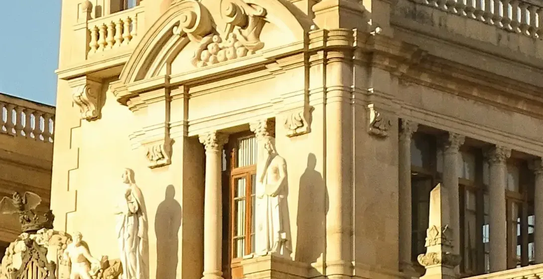 Detallada torre del reloj neobarroca del Ayuntamiento de Valencia bajo un cielo azul claro. Fachada de piedra con columnas, e