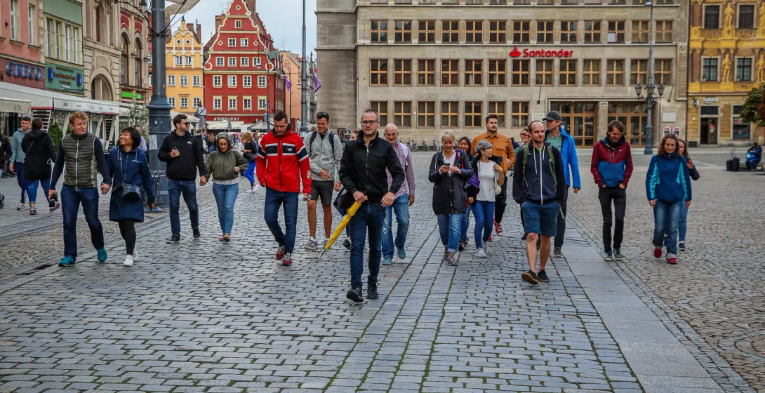 A group of people walks on a cobblestone street in Wroclaw Old Town, with historic buildings and a Santander bank in the back