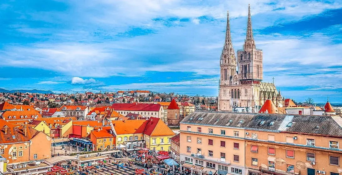 Panoramic view of Zagreb, Croatia, showing the Cathedral's spires, colorful rooftops, and a bustling market square.