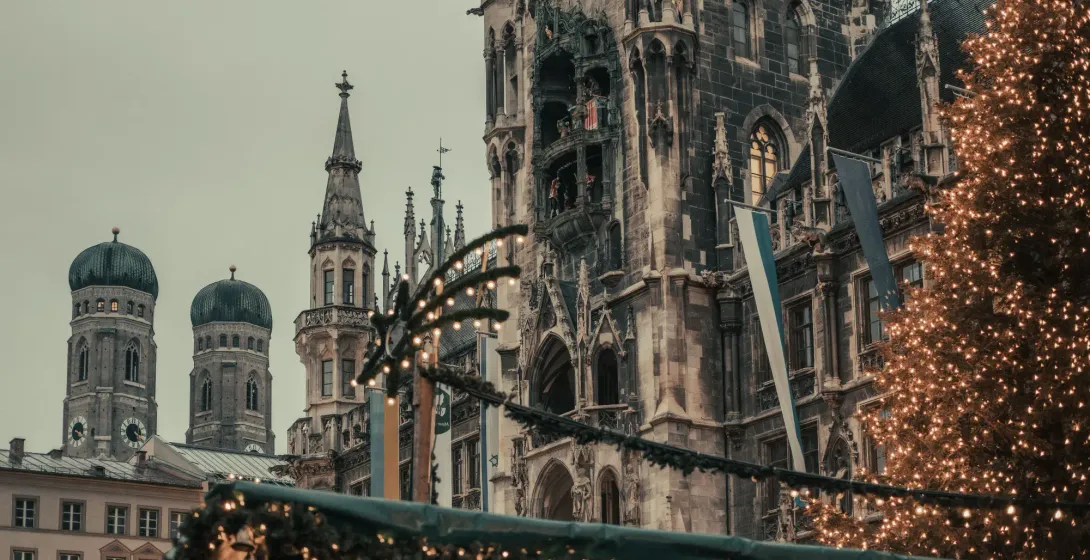 Münchner Neues Rathaus und Frauenkirche hinter beleuchtetem Weihnachtsbaum und Marktstand.
