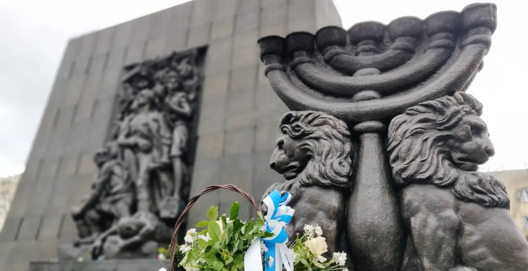 Pomnik Bohaterów Getta w Warszawie z menorą i kwiatami.