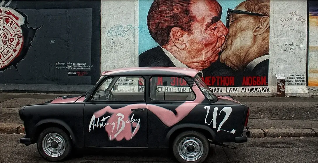 Samochód Trabant z graffiti zaparkowany w pobliżu słynnego muralu „Braterny Pocałunek” na East Side Gallery w Berlinie.