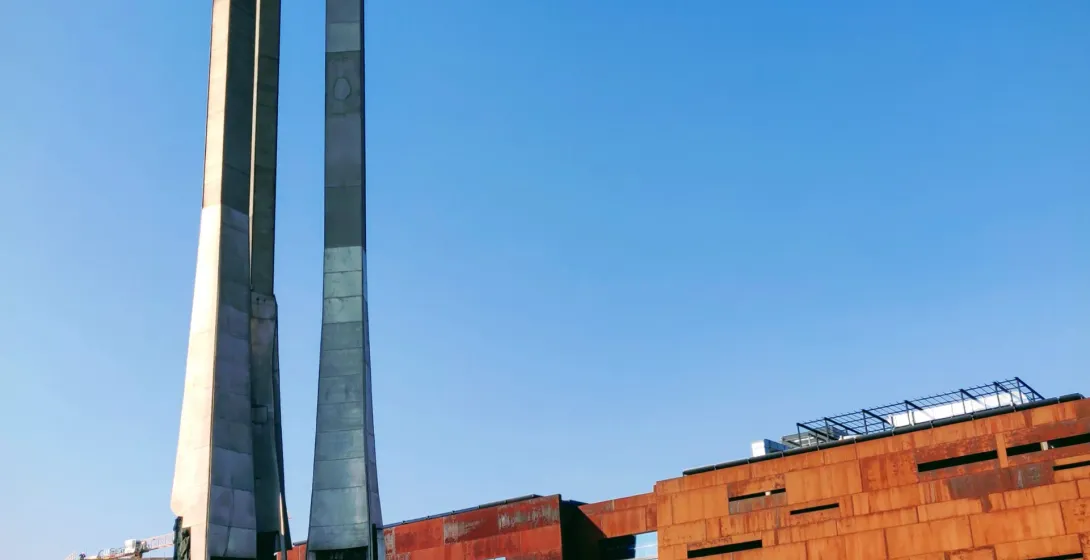 Monument to the Fallen Shipyard Workers 1970 in Gdańsk, with three tall crosses and anchors, next to a modern building wit...