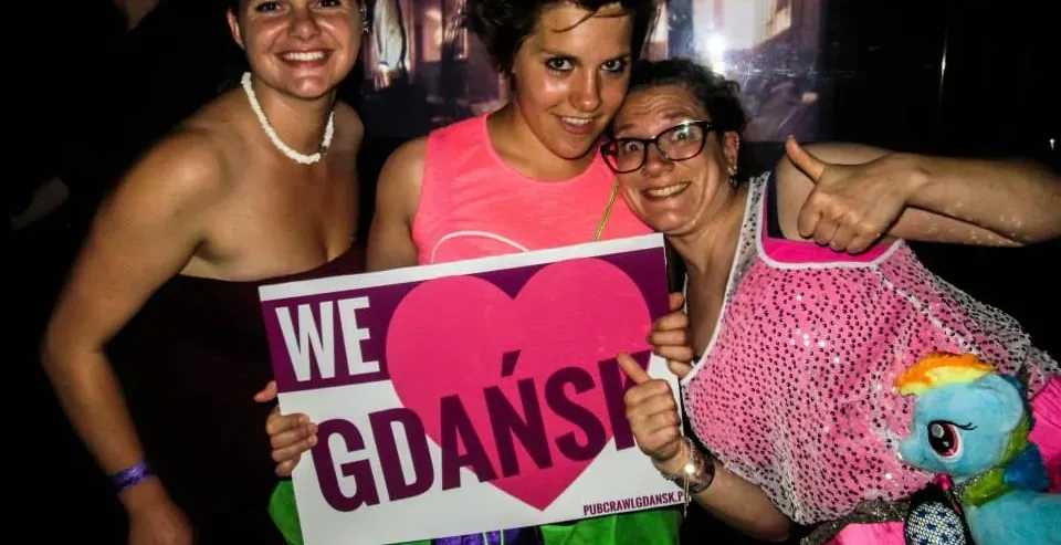 Trzy szczęśliwe turystki w Gdańsku, Polska, trzymające tabliczkę z napisem 'Kochamy Gdańsk'.