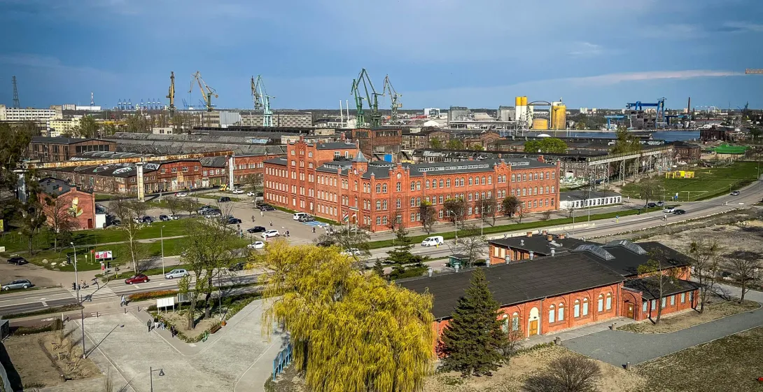 Widok z lotu ptaka na przemysłową dzielnicę portową Gdańska, z czerwonymi budynkami z cegły i parkiem.