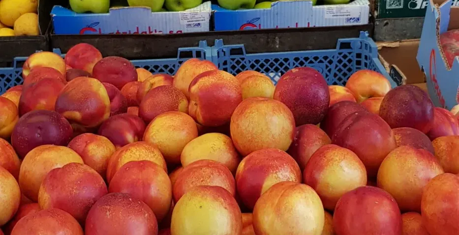 Un colorido puesto de frutas en un mercado griego, repleto de manzanas, naranjas y melocotones frescos.