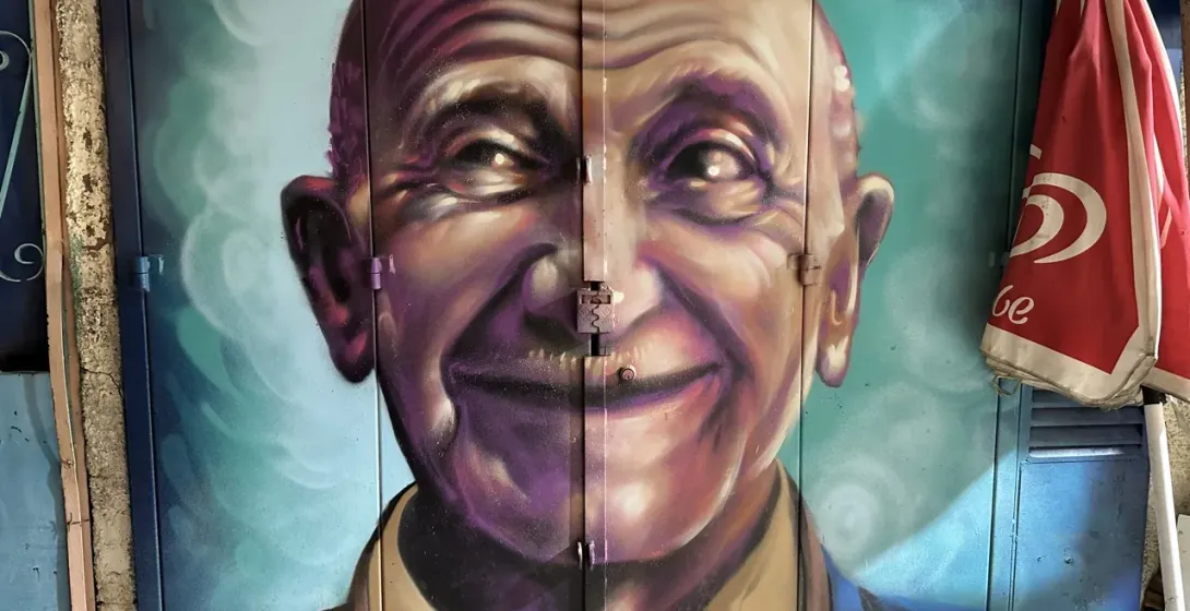 Lebhaftes Street-Art-Wandgemälde eines lächelnden älteren Mannes in Lissabon, Portugal.