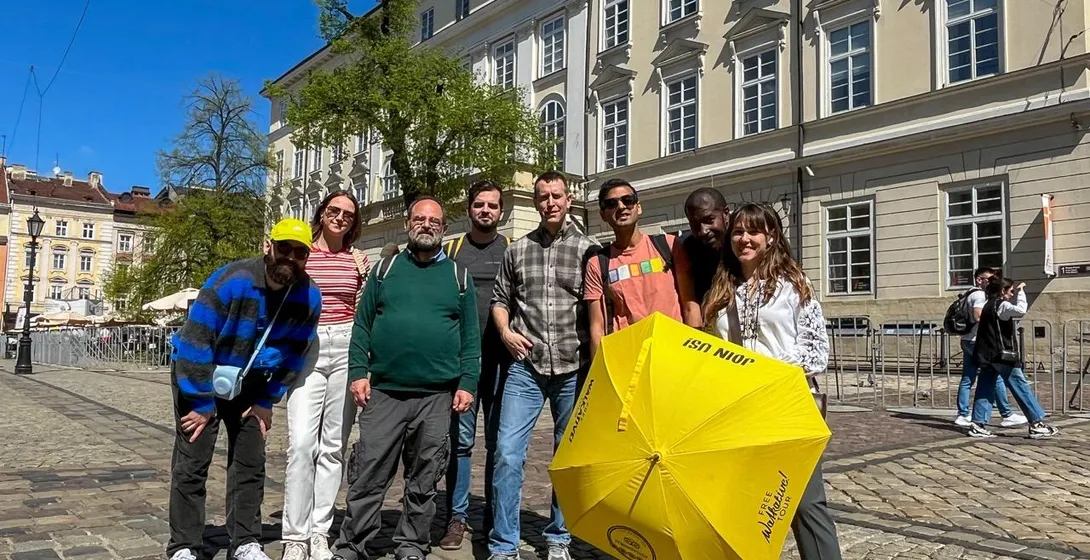 Eine vielfältige Gruppe von sieben Personen auf einer Kopfsteinpflasterstraße in Lwiw, mit einem Reiseleiter und einem gel...