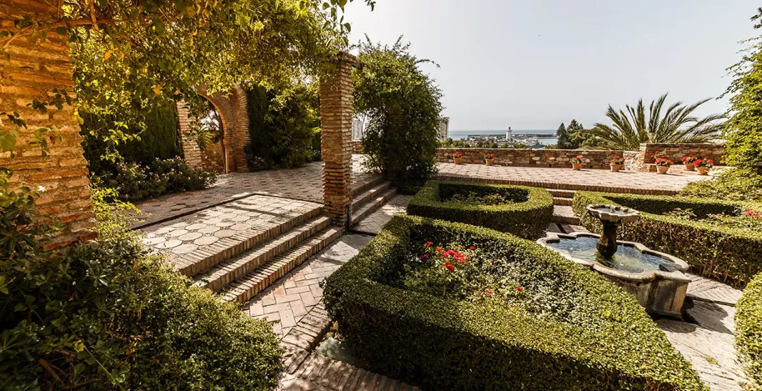 Sereno jardín en Málaga, España, con una fuente y vistas a la costa.